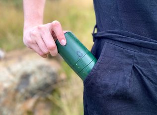 A green LU period kit being puled out of a womens pocket while she stands in a field 